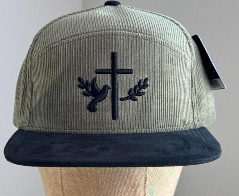 May include: A green corduroy baseball cap with a black brim. The cap features an embroidered design of a dove and a cross.