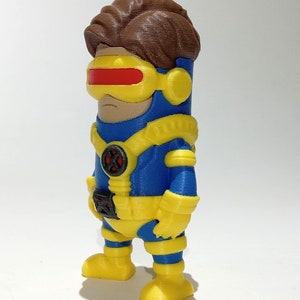 May include: A blue and yellow 3D printed figurine of a superhero with brown hair and a red visor.