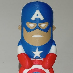 May include: A red, white, and blue 3D printed figurine of Captain America. The figurine is holding his shield in front of him. The shield has a white star in the center.