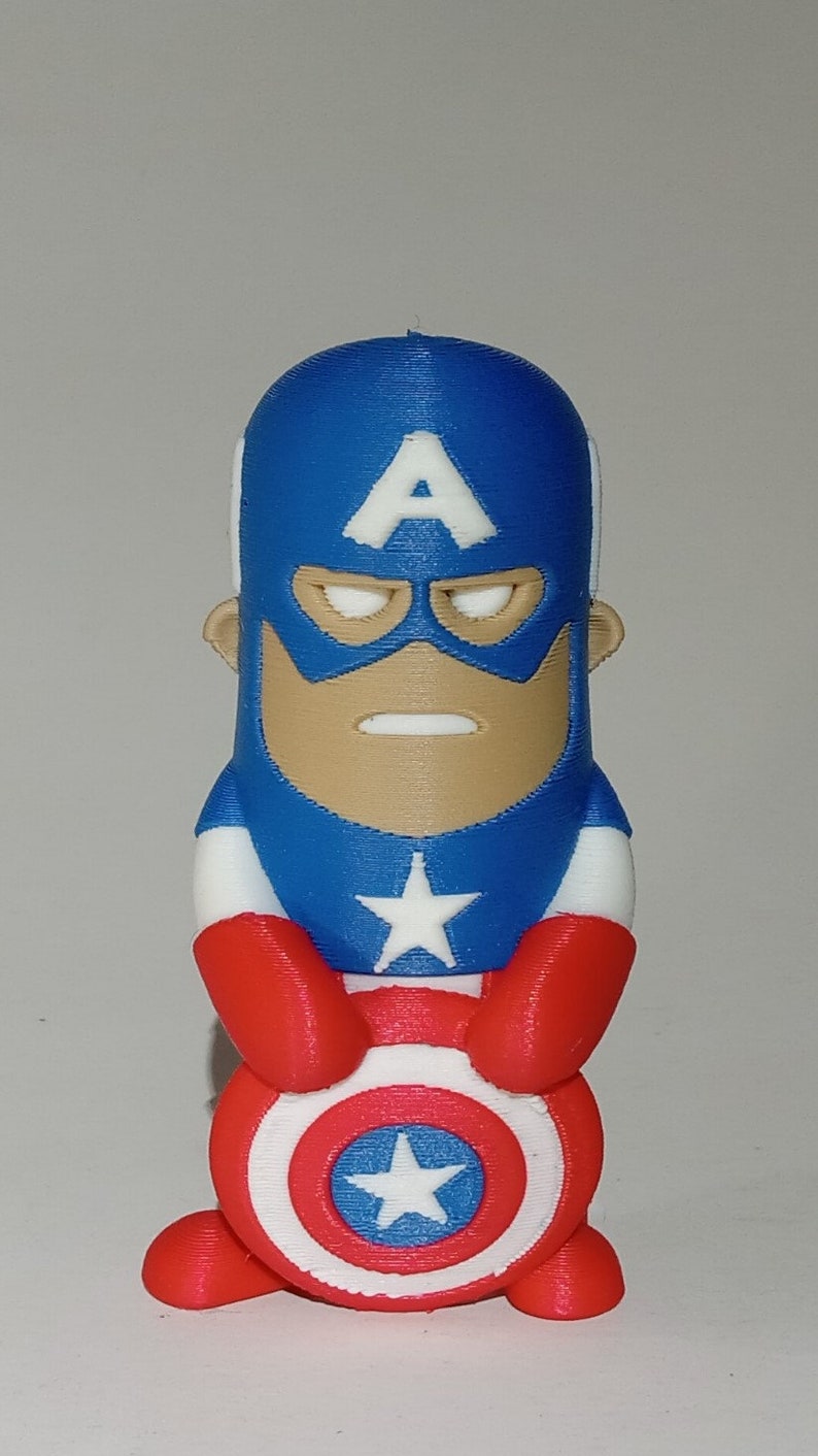 May include: A red, white, and blue 3D printed figurine of Captain America. The figurine is holding his shield in front of him. The shield has a white star in the center.