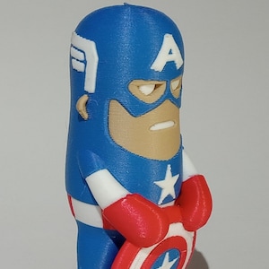 May include: A blue and red 3D printed figurine of Captain America holding his shield. The figurine is in a standing pose with a serious expression on its face. The shield is white with a red star in the center.