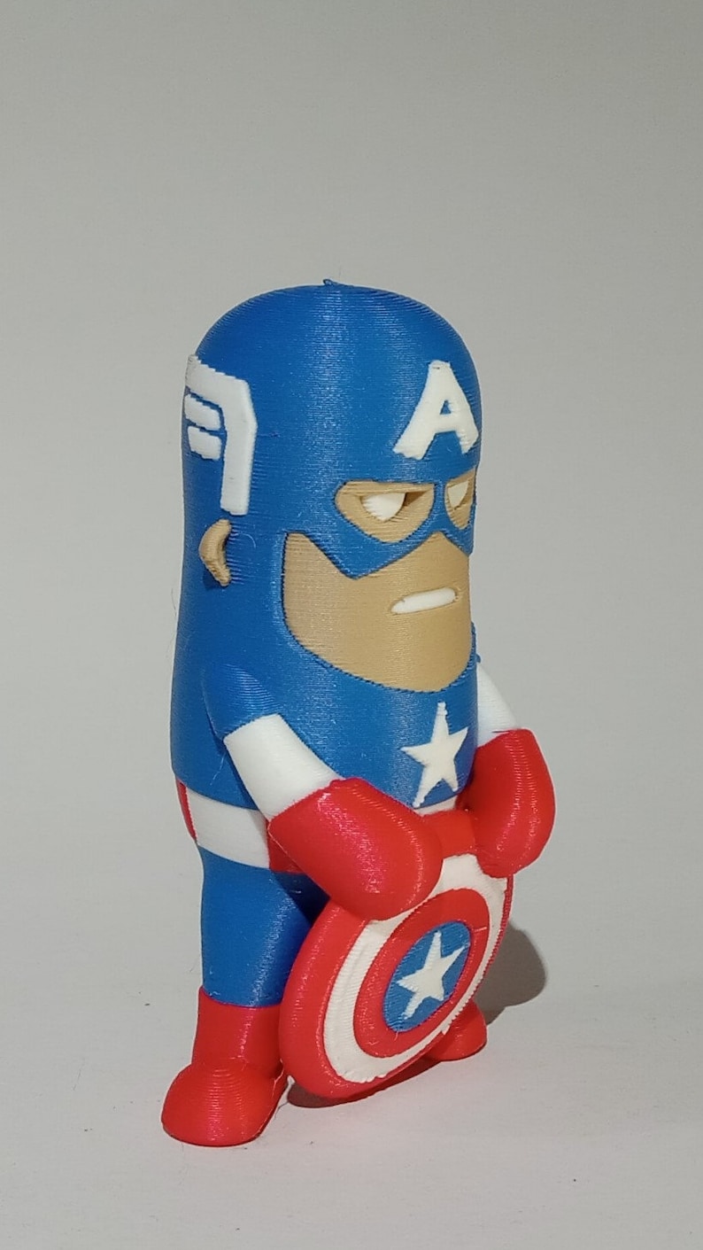 May include: A blue and red 3D printed figurine of Captain America holding his shield. The figurine is in a standing pose with a serious expression on its face. The shield is white with a red star in the center.