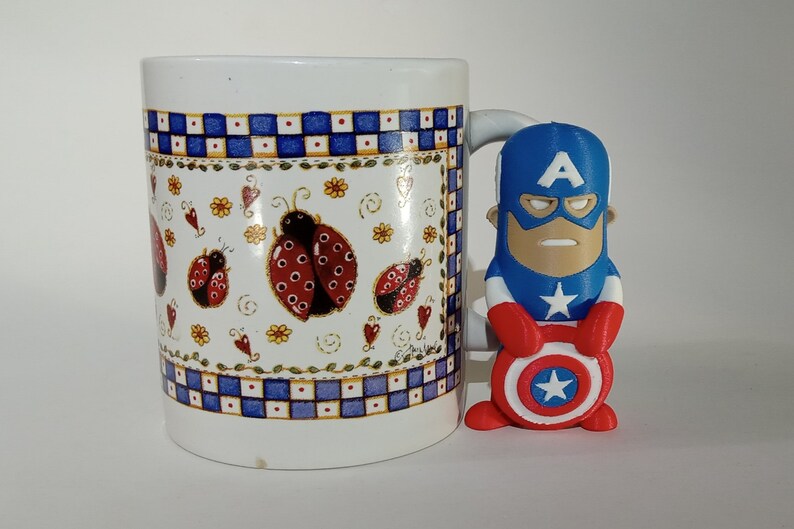 May include: A white ceramic mug with a blue and white checkered pattern and a ladybug design. A small red, white, and blue Captain America figurine is holding a red, white, and blue shield.