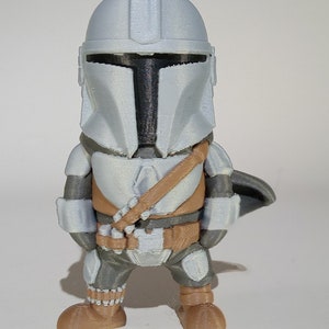 K&ouml;nnte beinhalten: Eine 3D-gedruckte Figur eines Mandalorianer-Charakters mit silbernem Helm und R&uuml;stung, einer braunen Brustplatte und einem passenden G&uuml;rtel. Die Figur hat einen kleinen Umhang und steht aufrecht.