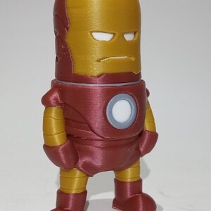 May include: A red and gold 3D printed figurine of Iron Man. The figurine is standing with its arms at its sides and has a serious expression on its face.