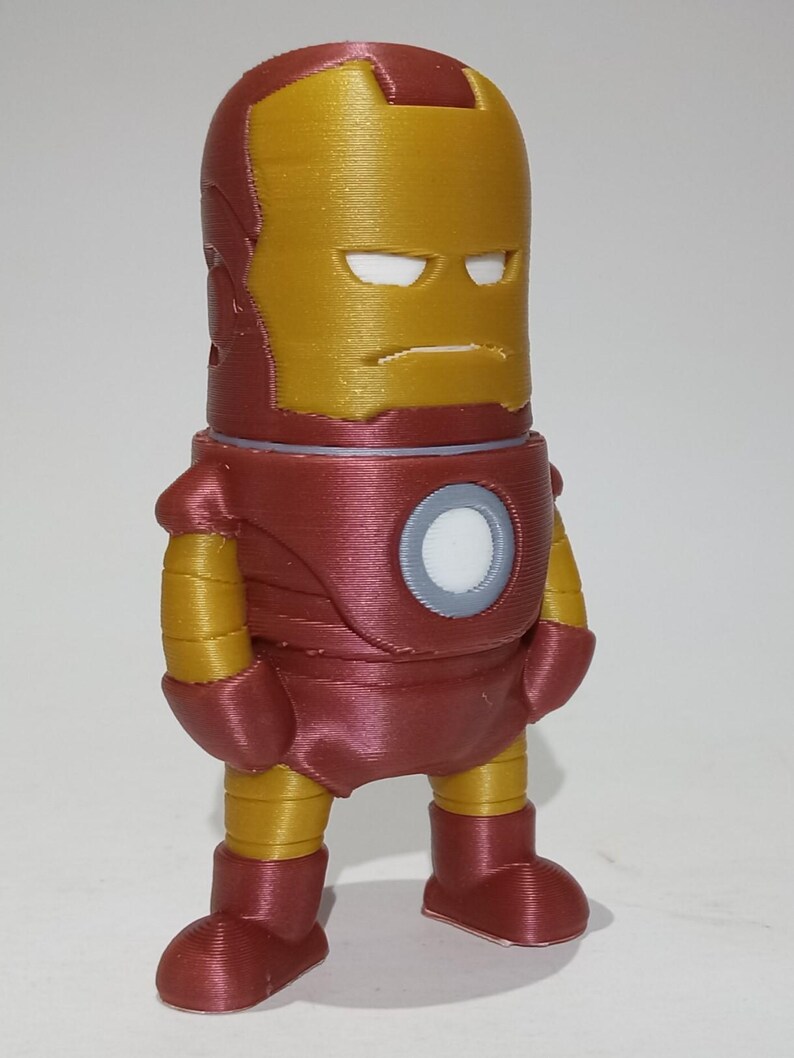 May include: A red and gold 3D printed figurine of Iron Man. The figurine is standing with its arms at its sides and has a serious expression on its face.