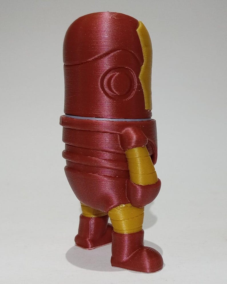 May include: A red and gold 3D printed figurine of a superhero. The figurine is standing with its arms at its sides and its legs slightly apart. The figurine has a red head and torso, with a gold face mask and gold accents on the arms and legs.
