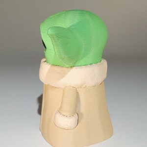 May include: A green and beige 3D printed figurine of a character from the Star Wars franchise. The character is wearing a robe and has large ears.