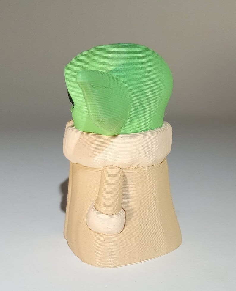 May include: A green and beige 3D printed figurine of a character from the Star Wars franchise. The character is wearing a robe and has large ears.