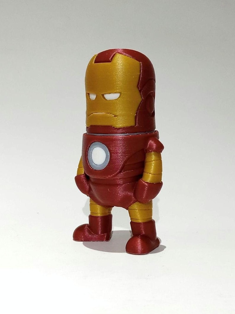 May include: A red and gold 3D printed figurine of Iron Man. The figurine is standing with its arms at its sides and has a serious expression on its face.