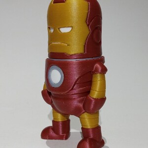 May include: A red and gold 3D printed figurine of Iron Man. The figurine is standing with its arms at its sides and has a serious expression on its face.