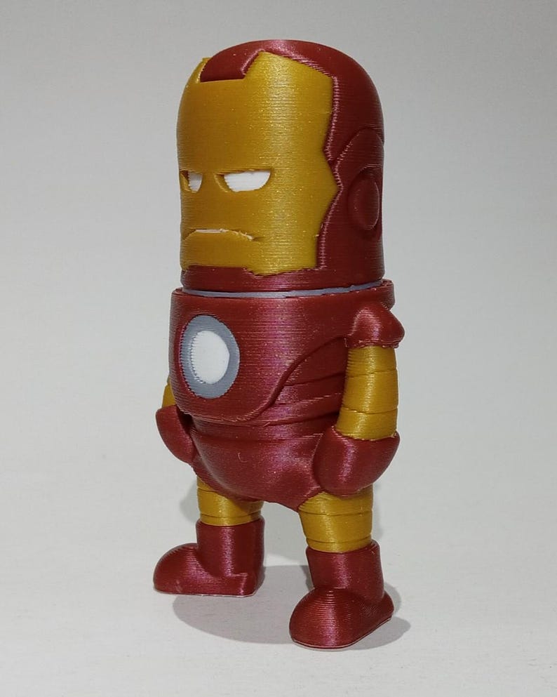 May include: A red and gold 3D printed figurine of Iron Man. The figurine is standing with its arms at its sides and has a serious expression on its face.