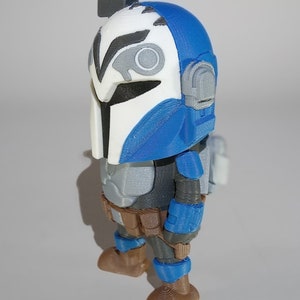 May include: A blue and white 3D printed action figure of a Mandalorian warrior. The figure is wearing a helmet with a visor and has a blaster rifle on its back.
