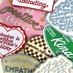 May include: A collection of embroidered fabric patches featuring various shapes and colors. Text includes Thank You for Including, Positive Energy, Inclusion is within everyone's ability, inclusion matters, Raise Kind Kids, Kind, Lead with Empathy, and Be Kind to all kinds.