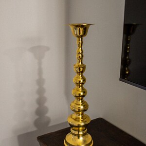 May include: A tall, gold metal candle holder with a round base and a series of decorative bulbs along the stem.
