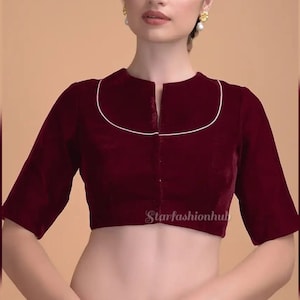 May include: A burgundy velvet blouse with a high, rounded neckline trimmed with white piping. The three-quarter sleeves and front closure add to the blouse's elegant design. The blouse is a rich, solid color.