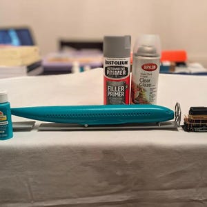 May include: A model airplane, a train, and various bottles of paint and primer. The airplane is blue and white, the train is black and gold, and the bottles are various colors.