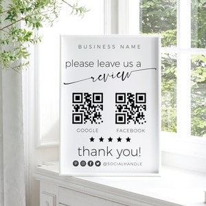 May include: White sign with black text that says "BUSINESS NAME please leave us a review" with two QR codes labeled "GOOGLE" and "FACEBOOK" below. There are five black stars below the QR codes and the text "thank you!" below the stars. There are social media icons below the text.
