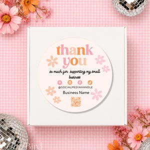 May include: A white square shipping box featuring a circular sticker with the text thank you, so much for supporting my small business, social media icons, @SOCIALMEDIAHANDLE, Business Name, and a QR code, decorated with pink flowers.