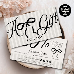 Puede incluir: Dos tarjetas de regalo con fondo a rayas y detalles de lazo negro. Las tarjetas dicen "Un regalo para ti" e incluyen información de contacto comercial. Una tarjeta ofrece un 20% de descuento en compras superiores a 30 €. Las tarjetas están sobre un plato decorativo.