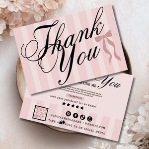 Puede incluir: Dos tarjetas rosas y blancas a rayas con texto "Thank You" en negro. Una tarjeta presenta una ilustración de lazo. La segunda tarjeta incluye iconos de redes sociales, un código QR y el texto "love your purchase? let us know!" y "TAKE A & TAG US ON SOCIAL MEDIA."