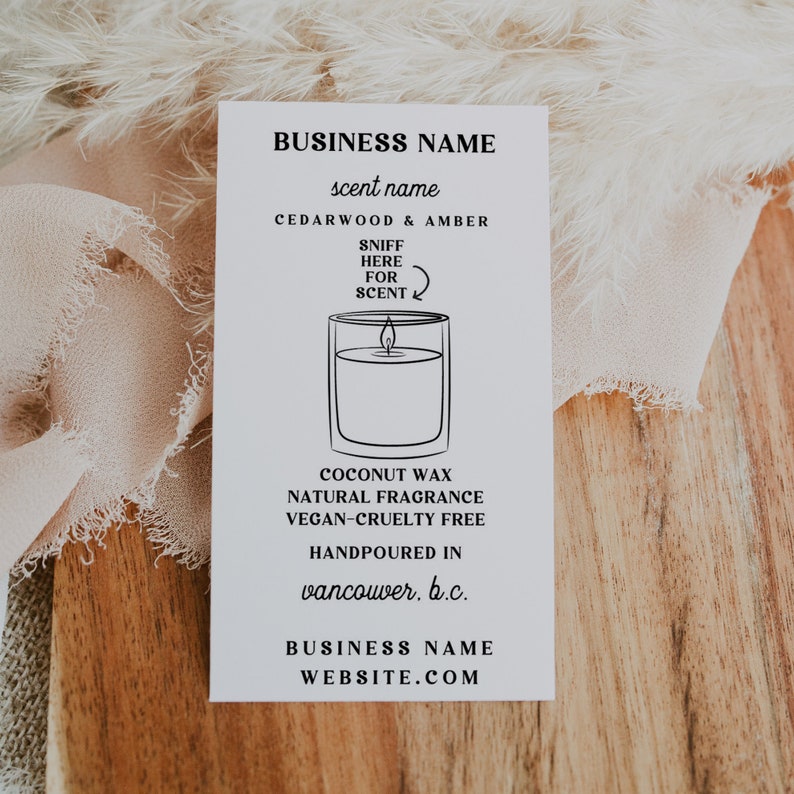 May include: A white label with black text and a line drawing of a candle. The text reads "BUSINESS NAME", "scent name", "CEDARWOOD & AMBER", "SNIFF HERE FOR SCENT", "COCONUT WAX NATURAL FRAGRANCE VEGAN-CRUELTY FREE", "HANDPOURED IN vancouver. b.c.", "BUSINESS NAME WEBSITE.COM".