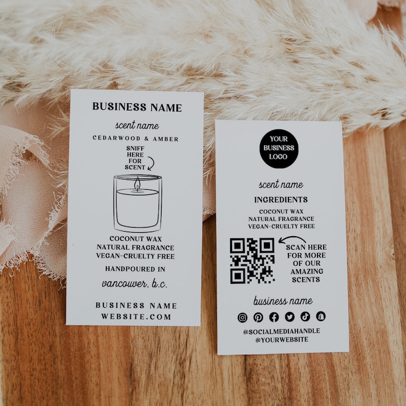 May include: Two white business cards with black text. The left card features a candle illustration and the text "BUSINESS NAME", "scent name", "CEDARWOOD & AMBER", "SNIFF HERE FOR SCENT", "COCONUT WAX NATURAL FRAGRANCE VEGAN-CRUELTY FREE HANDPOURED IN vancouver, b.c.", "BUSINESS NAME WEBSITE.COM". The right card features a QR code, the text "YOUR BUSINESS LOGO", "scent name", "INGREDIENTS COCONUT WAX NATURAL FRAGRANCE VEGAN-CRUELTY FREE", "SCAN HERE FOR MORE OF OUR AMAZING SCENTS", "business name", "@SOCIALMEDIAHANDLE @YOURWEBSITE".