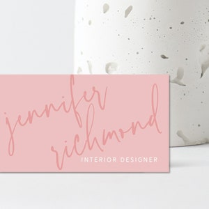 May include: A pink business card with the text "jennifer richmond" in a cursive font and the text "INTERIOR DESIGNER" in a smaller font.