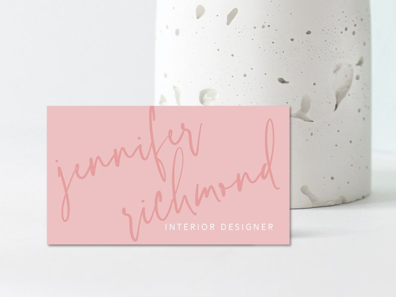 May include: A pink business card with the text "jennifer richmond" in a cursive font and the text "INTERIOR DESIGNER" in a smaller font.