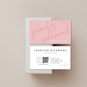 May include: A white business card with a pink border and a QR code. The text on the card reads "Jennifer Richmond, Interior Designer, Website.com, Email@email.com, 123-456-7890".
