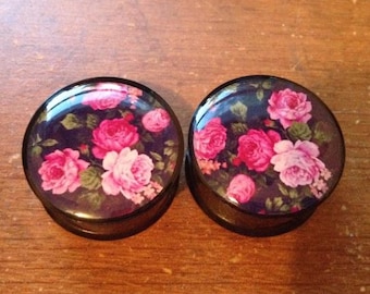 May include: Pair of black floral ear gauges with pink and white roses on a dark background.