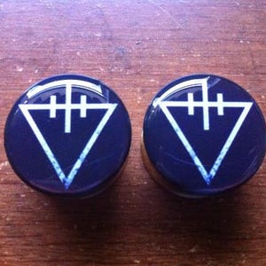 May include: Two black and white ear gauges with a triangle and three vertical lines design.