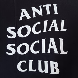 May include: Black t-shirt with the white text "ANTI SOCIAL SOCIAL CLUB" in a stacked arrangement. The text is in a bold, sans-serif font, and the shirt appears to be made of a soft material.