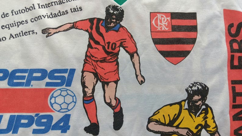 May include: White t-shirt with a red, black, and white soccer player graphic, a black and red crest with the letters "CR", and the text "PEPSI UP'94" in red, blue, and white. The text "ANTI EBS" is visible on the right side of the shirt.