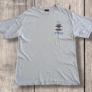 May include: Light gray t-shirt with a crew neck and short sleeves. The shirt features a colorful graphic of a sunset and the text "Rip Curl". The shirt is made of a soft, comfortable material.