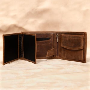 May include: Open brown leather wallet with multiple compartments, including card slots, a zippered pocket, and a billfold. The wallet is displayed open, revealing its interior and construction. The leather has a distressed appearance.
