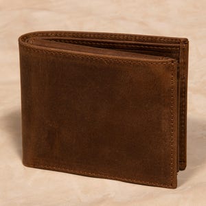 May include: A brown leather bi-fold wallet. The wallet is rectangular with rounded corners and a stitched edge. The leather has a distressed appearance, with variations in color and texture. The wallet is open, revealing the interior compartments.