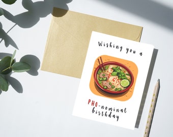 Op de afbeelding: Een witte kaart met een cartoonillustratie van een kom pho, een Vietnamese noedelsoep. De tekst op de kaart luidt "Wishing you a PHO-nominal birthday."