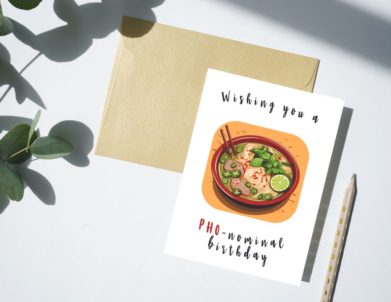 Puede incluir: Una tarjeta blanca con una ilustraci&oacute;n de dibujos animados de un taz&oacute;n de pho, una sopa de fideos vietnamita. El texto en la tarjeta dice "Wishing you a PHO-nominal birthday."