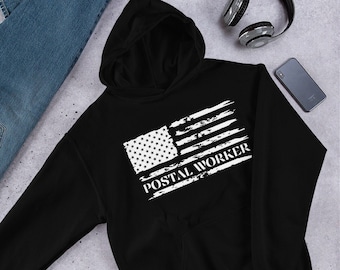 Puede incluir: Sudadera con capucha negra con una bandera estadounidense blanca desgastada y el texto "POSTAL WORKER" impreso en la parte delantera.