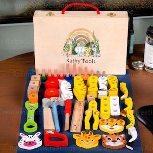 May include: Wooden toy tool set with a light brown wooden box featuring a red handle and the text "Kathy'Tools". The set includes various colorful wooden tools and animal-shaped pieces, arranged on a blue surface.