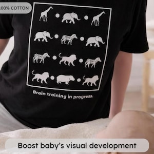 May include: Black t-shirt with a white square containing animal illustrations, including giraffes, elephants, and zebras. The text "Brain training in progress" is below the square. The shirt is made of 100% cotton.
