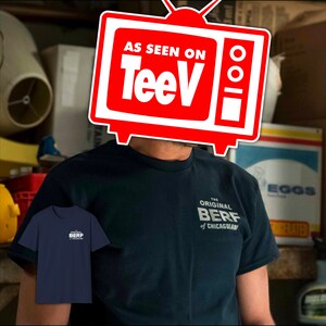 May include: A man wearing a dark blue t-shirt with the text "The Original Berf of Chicagoland" printed on the front. The man is wearing a red television-shaped sticker over his head that says "As Seen On TeeV".