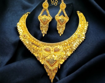 May include: A gold necklace and earrings set with intricate designs. The necklace is a crescent shape with a pendant in the center. The earrings are long and dangle.