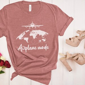 May include: A dusky pink t-shirt with the words "Airplane mode" and a graphic of a plane over a world map. A pair of platform heels in a light tan colour are next to the shirt. A bouquet of flowers is in the lower left corner.
