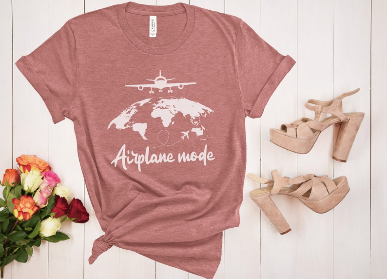 May include: A dusky pink t-shirt with the words "Airplane mode" and a graphic of a plane over a world map. A pair of platform heels in a light tan colour are next to the shirt. A bouquet of flowers is in the lower left corner.