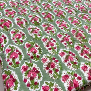 May include: Green fabric with a white and pink floral pattern. The fabric has a subtle sheen and is perfect for quilting or crafting.
