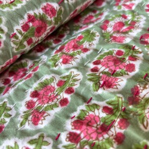 May include: Close-up of a green fabric with a white background and a pink floral pattern. The fabric is quilted with pink thread.
