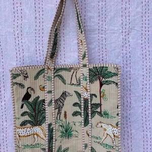 May include: A beige canvas tote bag with a jungle animal print. The print features zebras, leopards, toucans, and palm trees. The bag has brown and white striped handles.