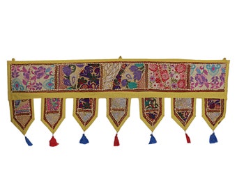 May include: A decorative wall hanging with a yellow border and colorful patchwork squares. Each square features floral and paisley designs in shades of pink, purple, and blue. The hanging has tassels in red and blue.